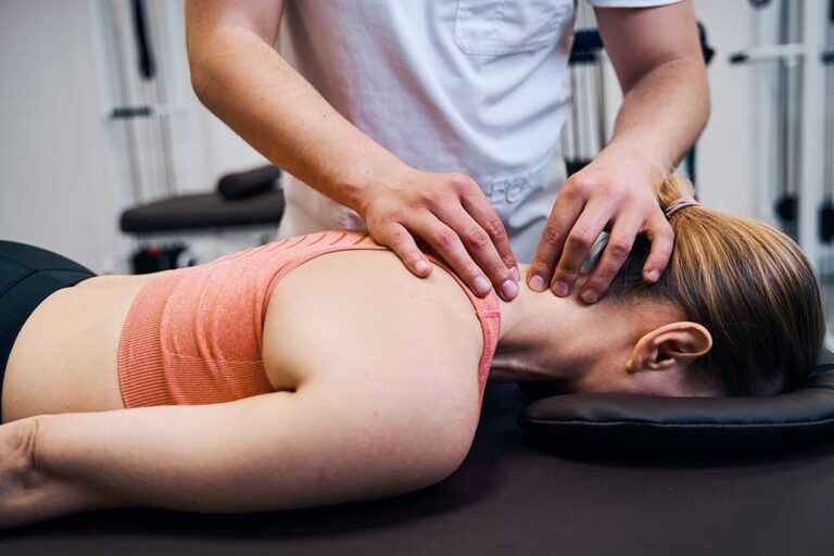 Person seated on an exam table while a clinician checks leg strength and sensation.